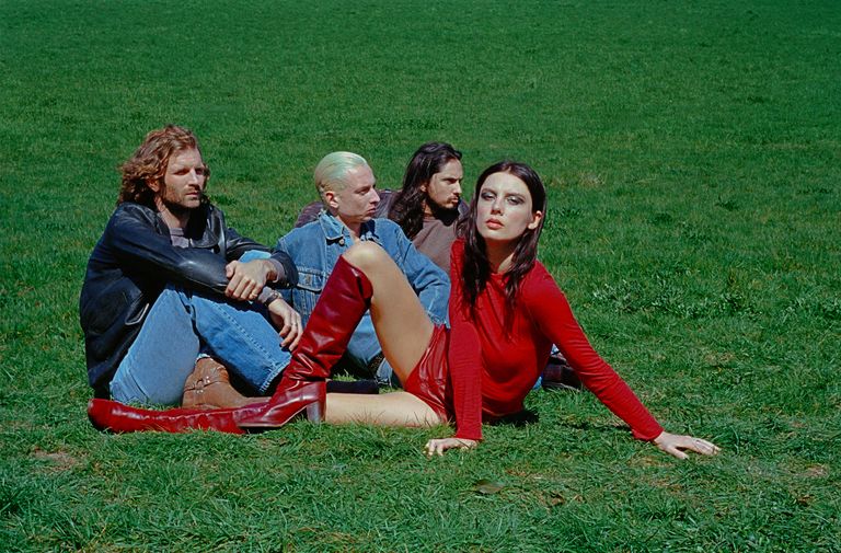 English alt-rock band Wolf Alice lounging on a grassy lawn in a promotional photo captured by photographer Rachel Fleminger Hudson.